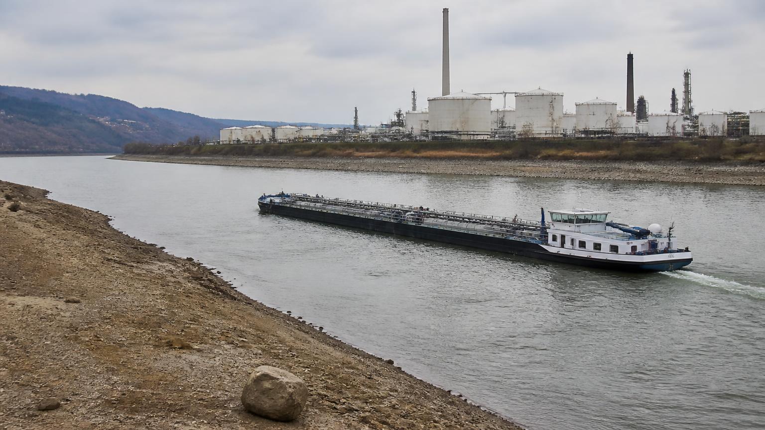 Inland fuel barge navigating waterway near refining and storage terminal infrastructure.